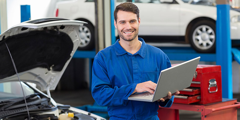 A mechanic using MAM Autowork Online on a laptop in a garage